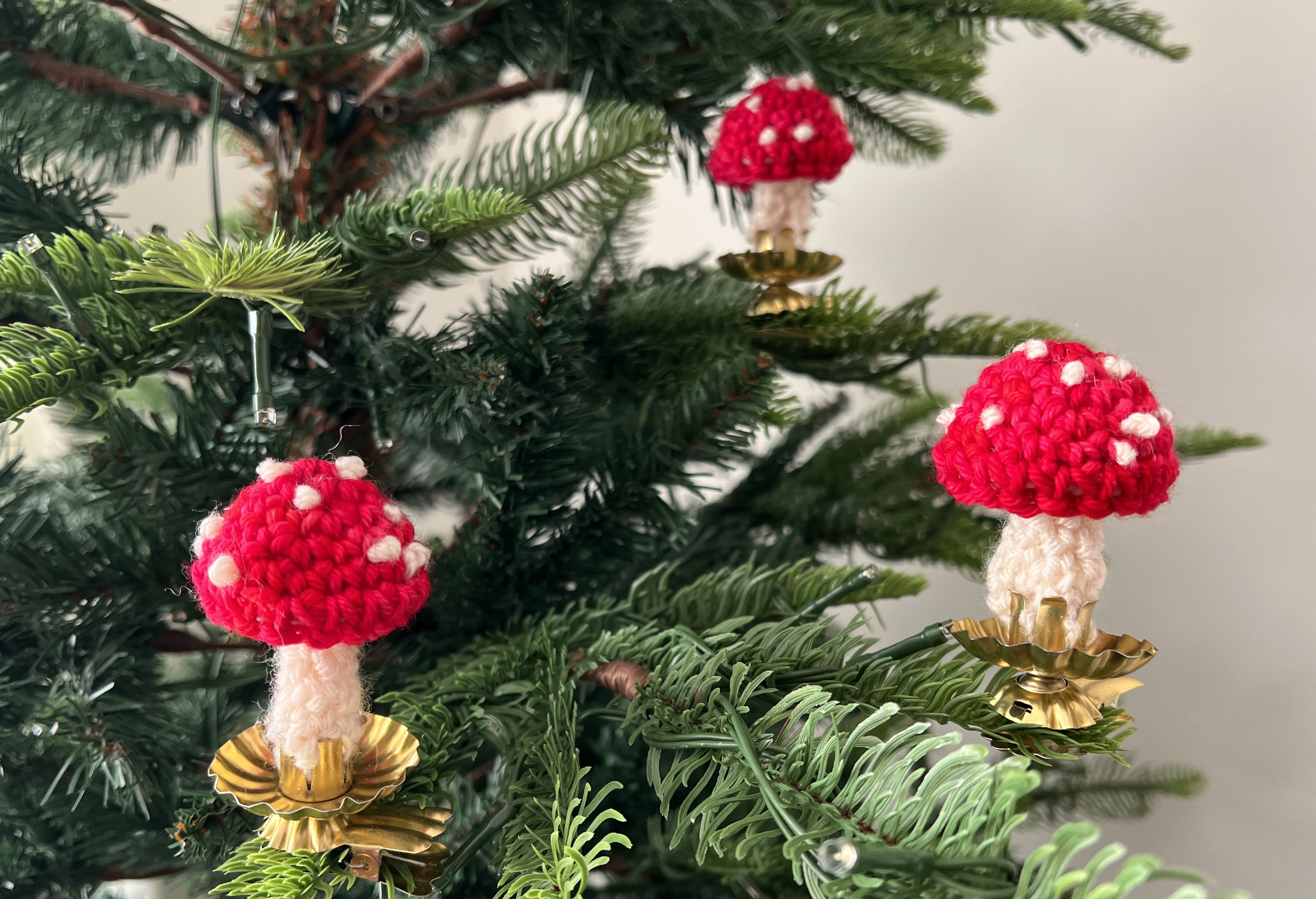 image of 3 small crocheted red and white toadstools clipped onto a christmas tree with candle clips